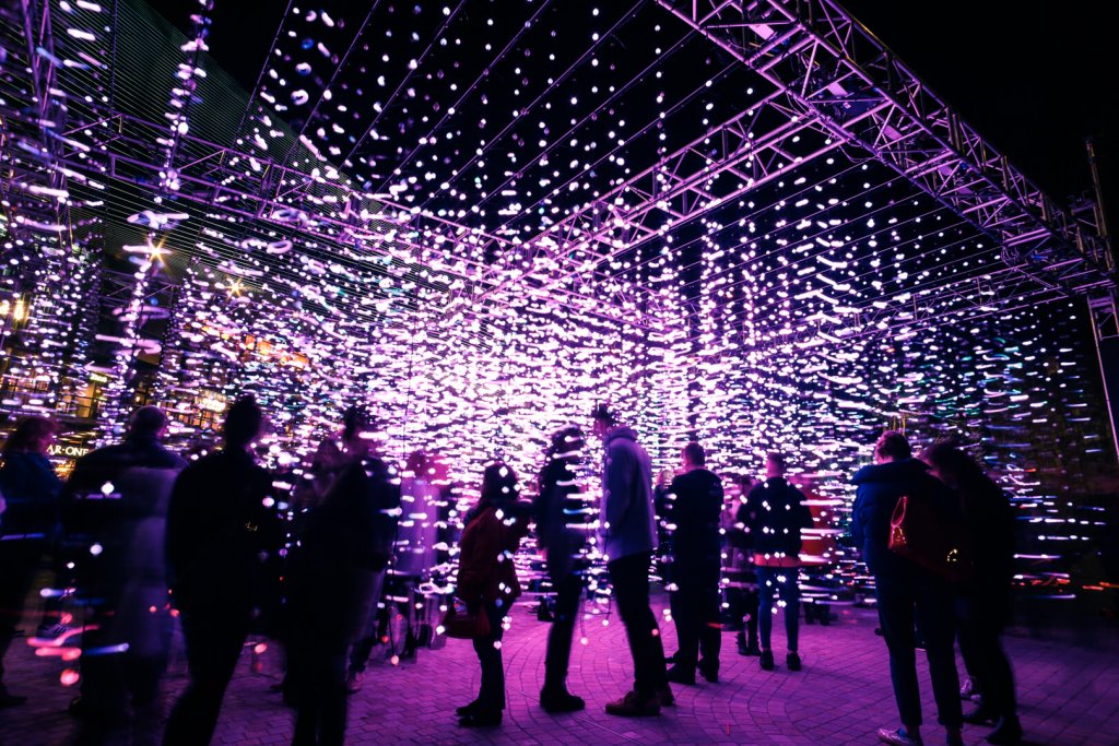 A photograph of a group of people under a set of lights on string, with a pink glow